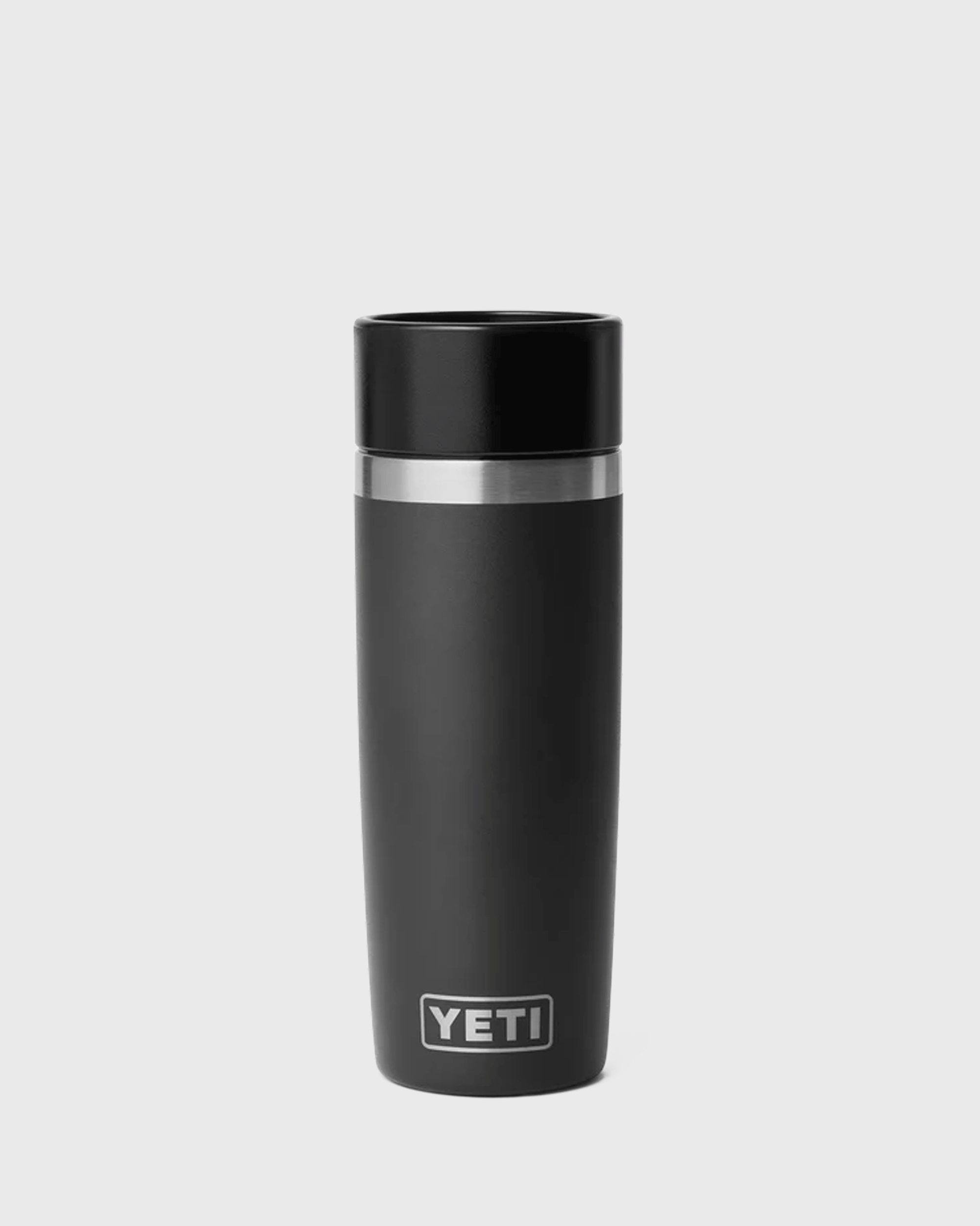 A YETI insulated travel tumbler in matte black with a stainless steel band and a white YETI logo near the base, shown on a light gray background.
