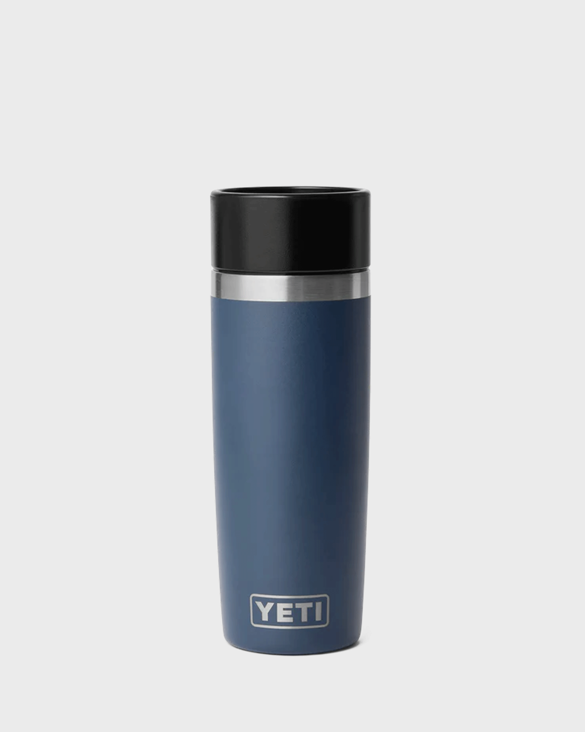A YETI insulated travel tumbler in slate blue with a black lid and a silver stainless steel band near the top, shown on a light gray background.